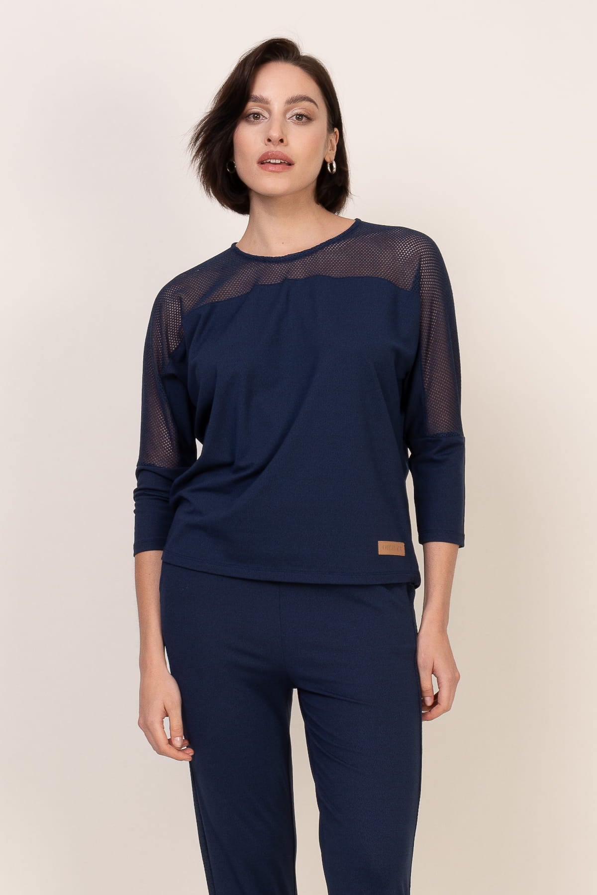 Kobieta z krótkimi brązowymi włosami nosi Loungewear wiskozowa bluzka z siateczką - ciemne dżinsy i pasujące granatowe spodnie, stojąc na prostym jasnym tle.